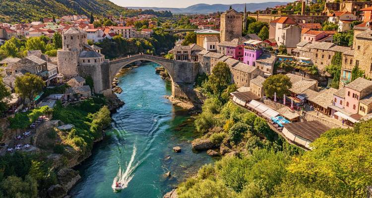 Sonnendurchflutete Aussicht auf Mostars ikonische Steinbogenbrücke, die einen türkisfarbenen Fluss überspan.