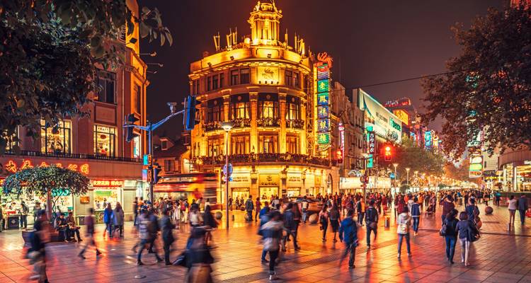 Bustling pedestrian shopping street illuminated by neon lights and historic building facades at night