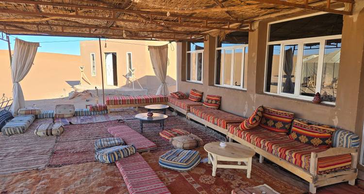 Acogedora sala de estar del campamento desértico con asientos bajos acolchados, alfombras y paredes abiertas con vistas a la arena.
