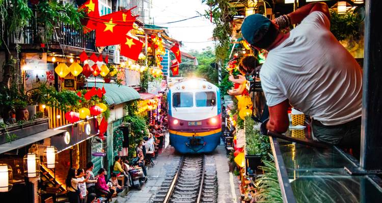 Kleurrijke scène op Hanoi's Trainstraat terwijl een locomotief op een paar centimeter afstand langs cafes en toeschouwers raast.