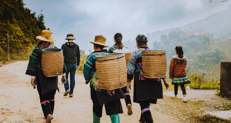 Lokale vrouwen in traditionele kleding dragen geweven manden terwijl ze langs een landelijke onverharde weg in mistig berglandschap wandelen.
