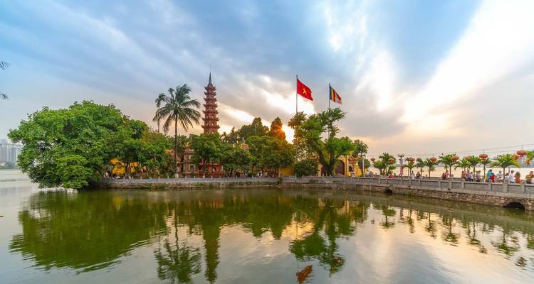 Tran Quoc Pagoda en Vietnamese vlaggen weerspiegeld in stil meerwater bij zonsopgang met dramatische wolken.