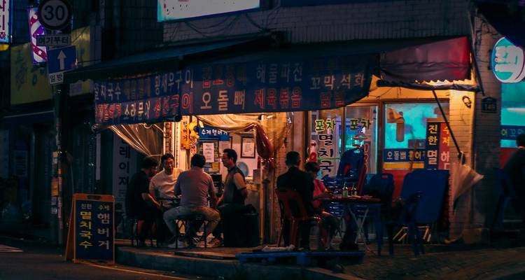 Klein Koreaans straatrestaurant met gasten die 's nachts onder neonborden zitten.