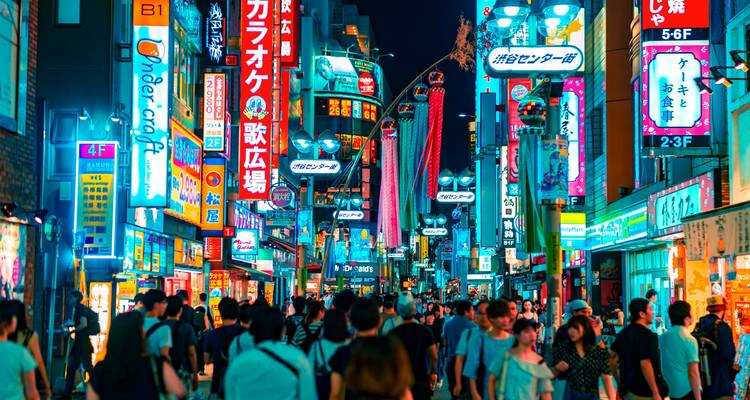 Drukke verlichte straat in Tokyo met felle billboards en voetgangers.