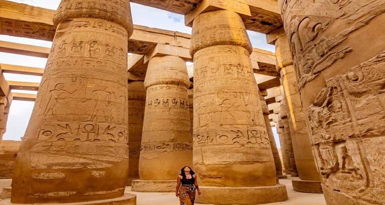 Un visiteur se tient, éclipsé par d'énormes colonnes couvertes de hiéroglyphes à l'intérieur du Temple de Karnak.