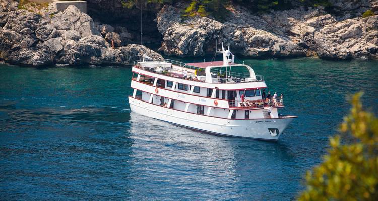 Kleines weißes Kreuzfahrtschiff, das durch klares türkisfarbenes Adriatisches Meer neben einer felsigen Küstenlinie segelt.