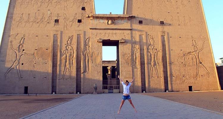 Une personne saute avec joie devant les murs massifs du pylône couverts de hiéroglyphes au temple d'Edfou.