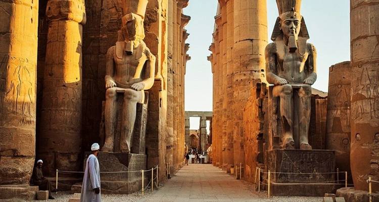 La lumière dorée baigne les statues imposantes et les colonnes du temple de Louxor tandis que les visiteurs se promènent dans l'allée.