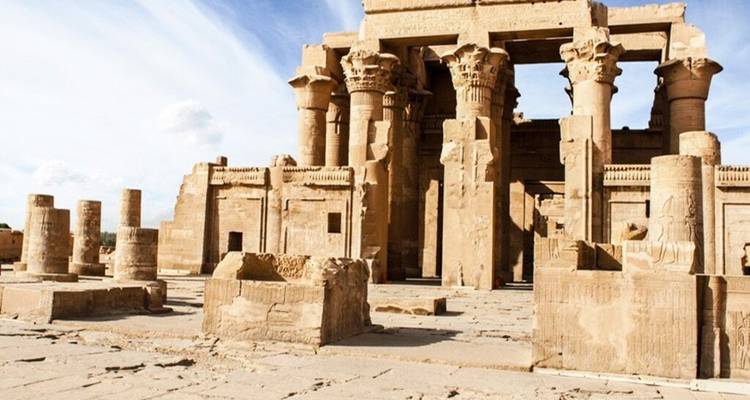 Salle hypostyle en pierre du Temple de Kom Ombo avec d'énormes colonnes sculptées contre un ciel bleu strié.