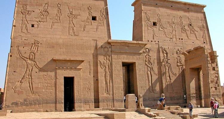 Les deux pylônes du Temple de Philae richement sculptés de divinités, s'élevant au-dessus d'une cour en pierre où les touristes explorent les lieux.