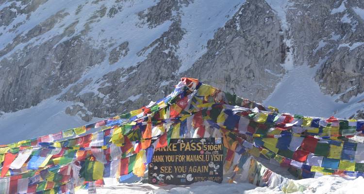 Banderas de oración ondeando en el letrero del Paso Larkya La nevado rodeado de escarpados picos del Himalaya.