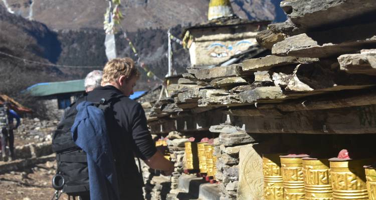 Los trekkers hacen girar filas de ruedas de oración doradas incrustadas en una pared de piedra en un pueblo del Himalaya.