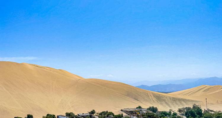 Vast expanse of rolling golden sand dunes beneath a clear blue sky in coastal Peru.