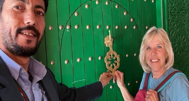 Selfie van een stel dat een sierlijk koperen deurklopper aanraakt op een grote groene deur met decoratieve studs.