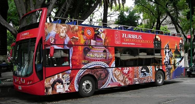 Heller roter Turibus-Doppeldeckerbus zur Besichtigung von Sehenswürdigkeiten, geparkt unter belaubten Bäumen entlang einer Stadtstraße.