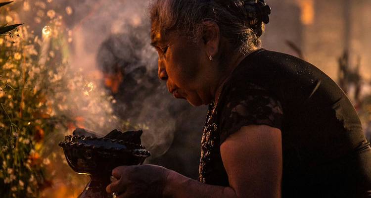 Femme âgée soufflant la fumée d'encens lors d'un rituel traditionnel dans une lumière chaude et tamisée