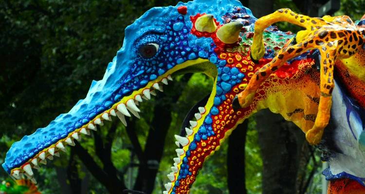 Sculpture de reptile alébrijes mexicain aux couleurs vives avec les mâchoires ouvertes exposée à l'extérieur parmi les arbres verts.