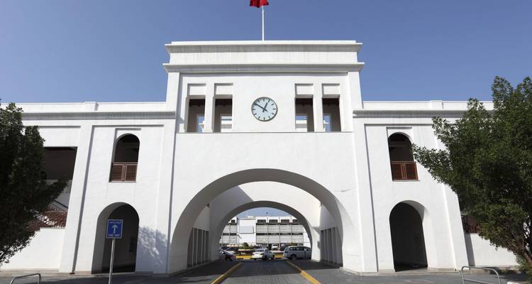 White gateway of Bab Al Bahrain with clock and national flag against clear sky.