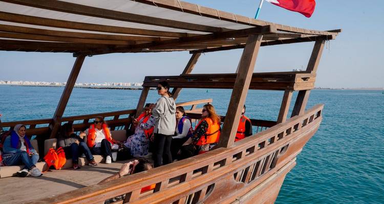 Group of tourists seated on a wooden dhow enjoying a sunny boat trip on blue waters.
