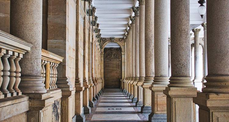 Interior de columnata neoclásica grandioso con pilares de piedra repetidos y techo ornamentado en Karlovy Vary.