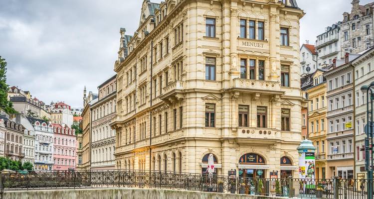 Fachadas elegantes del siglo XIX alineadas a lo largo de un canal y un puente peatonal en Karlovy Vary bajo cielos grises.