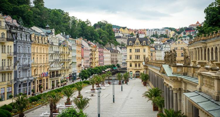 Paseo amplio flanqueado por edificios de spa ornamentados y casas adosadas en tonos pastel en Karlovy Vary en un día tranquilo.