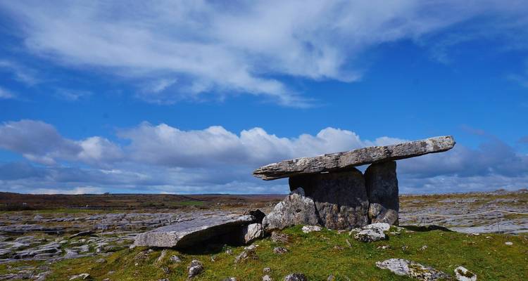 El antiguo dólmen de Poulnabrone de pie en un paisaje rocoso de piedra caliza bajo un cielo azul brillante.