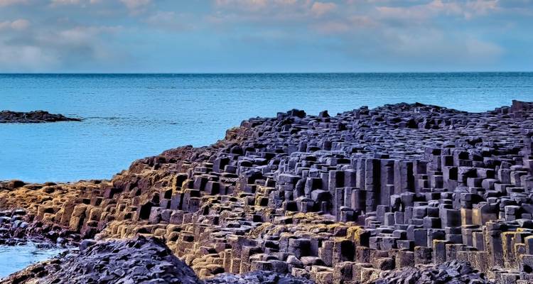 Columnas de basalto de la Calzada del Gigante extendiéndose hacia el tranquilo Océano Atlántico Norte de aguas azules.
