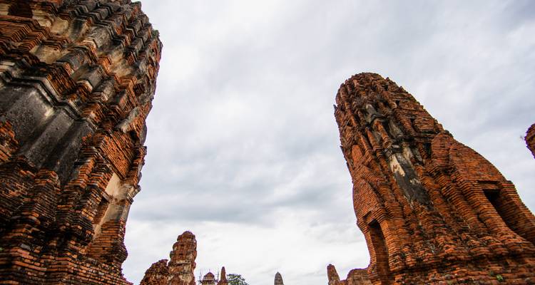 Laaghoekig zicht op imposante bakstenen stupas van Ayutthaya die naar een grijze lucht reiken.