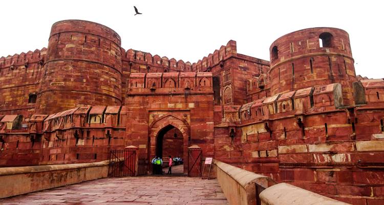 Bezoekers gaan door de gigantische rode zandsteenpoort van Agra Fort terwijl een vogel boven hen voorbijglijdt.