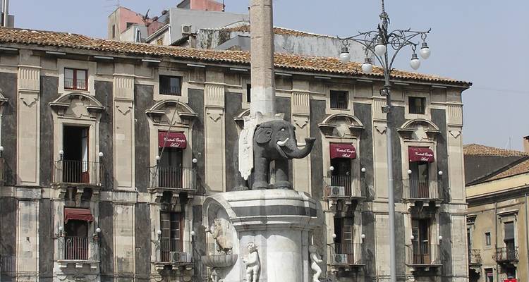 La fontaine éléphant emblématique de Catane se dressant devant des bâtiments baroques ornés noir et blanc.