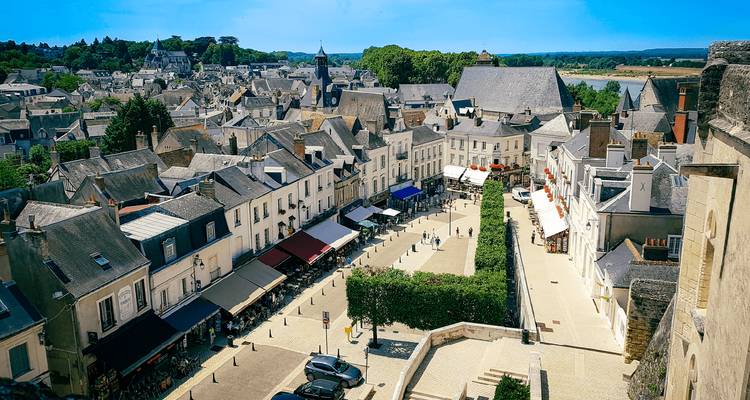 Aerial view over a quaint French town square with slate-roofed houses, shop awnings and narrow stone streets.