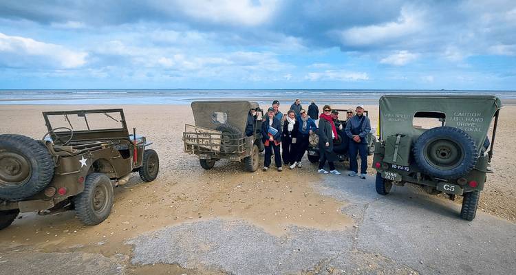 Small group posing beside vintage military jeeps on a wide sandy beach under a dramatic sky.