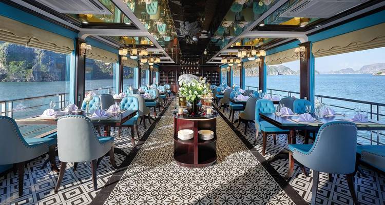 Luxurious, empty cruise dining hall with patterned tiles, blue chairs, and large windows framing Halong Bay.