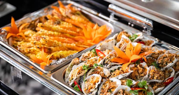 Close-up of buffet trays filled with grilled prawns and oysters garnished with orange carrot flowers.