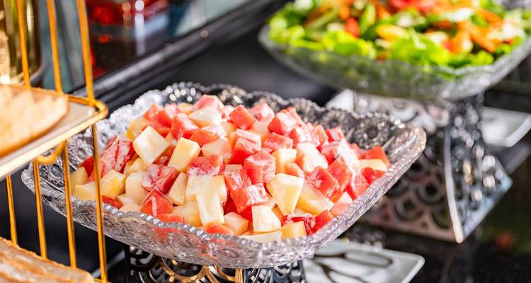 Glass dish of neatly cubed melon and watermelon salad on a buffet counter.
