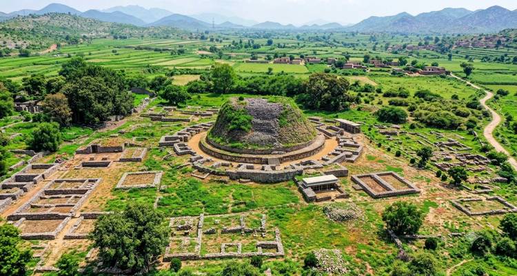 Luchtfoto van de oude Dharmarajika stupa ruïnes omgeven door groene velden en bergen in de verte in Taxila.