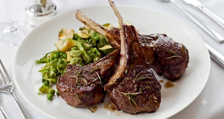 Gourmetbord met gegrilde lamskoteletjes garneerd met rozemarijn, geserveerd met groene groenten.