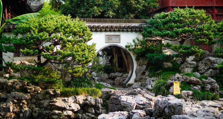 Scène classique de jardin chinois avec une porte lune circulaire située parmi des rochers sculptés et des pins.