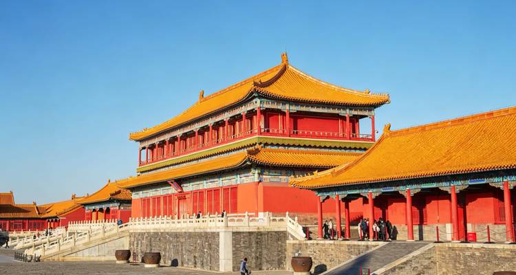 Les halls brillamment éclairés de la Cité interdite de Pékin avec ses murs rouge vif et ses toits dorés sous un ciel bleu dégagé.