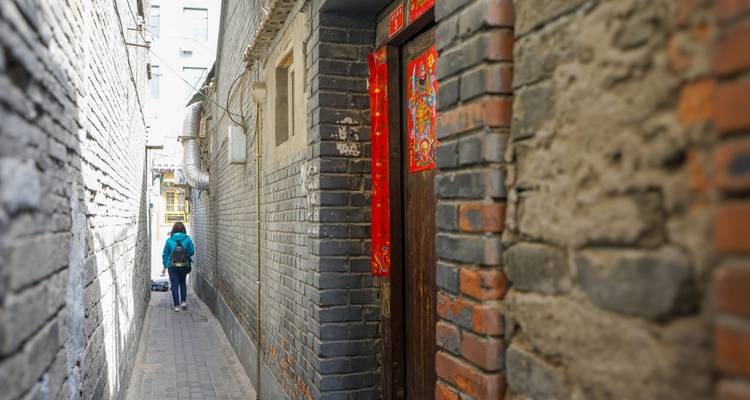 Ruelle hutong étroite en briques avec un piéton se dirigeant vers la lumière du jour éclatante.