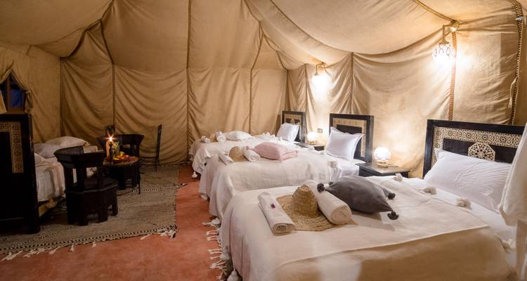 Interior acogedor de tienda de campamento en el desierto con varias camas bien hechas, iluminación suave y decoración tradicional.
