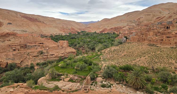 Un amplio valle rocoso con pueblos dispersos de adobe y un exuberante oasis verde de árboles que atraviesa el centro.
