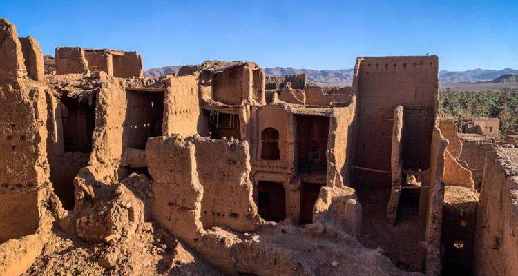 Vervallende adobemuren en torens van een oud kasbah staan afgetekend tegen een helder blauwe woestijnhemel.