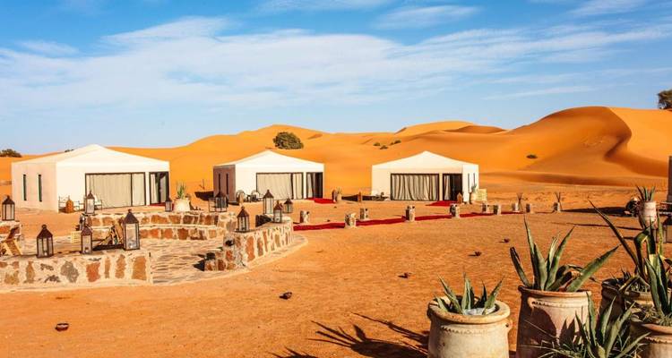 Luxe witte canvas tenten die rond een stenen patio in het midden van gouden woestijnzandduinen onder een blauwe hemel zijn gerangschikt.