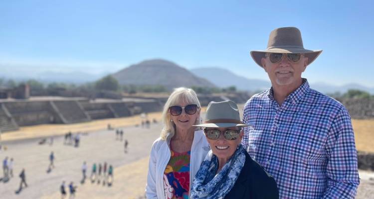 Drei Besucher posieren vor der Pyramide des Mondes von Teotihuacán und dem großen Platz im Hintergrund.