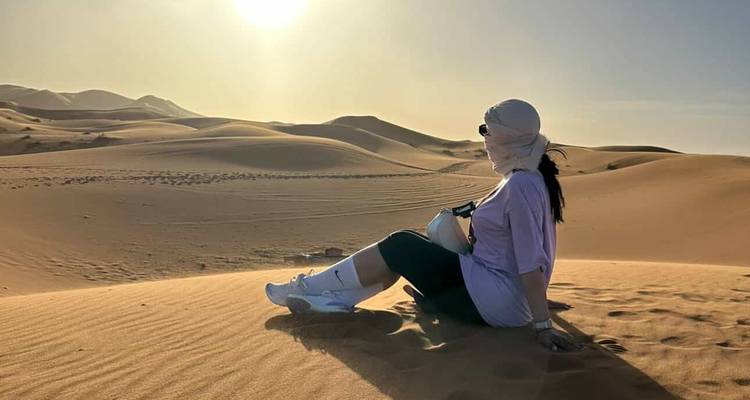 Mujer sentada en una duna del Sahara bañada de sol al atardecer, observando las arenas ondulantes.