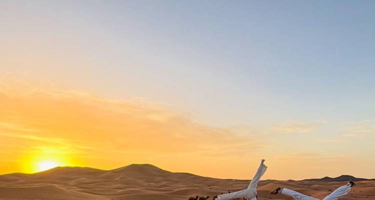 Amanecer dorado sobre las dunas infinitas del Sahara con siluetas de camellos y jinetes por debajo del horizonte.