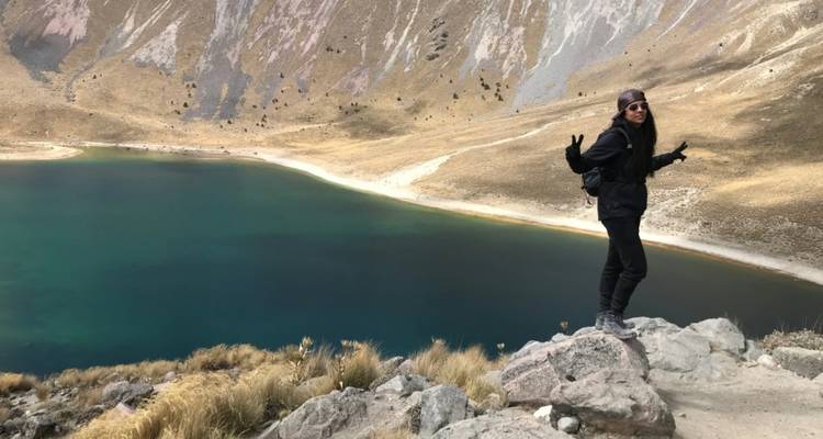 Wanderer, der auf einem felsigen Grat posiert und auf den türkisfarbenen Kratersee des Nevado de Toluca blickt.
