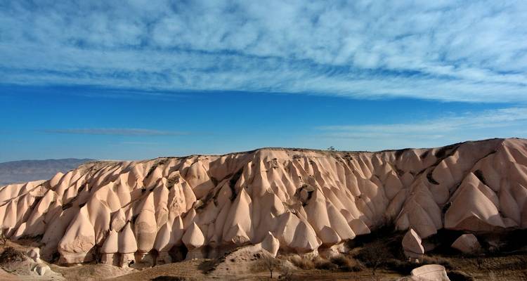 Golvormige roze rotsformaties van Cappadocië onder een wijde blauwe lucht met lichte wolken.